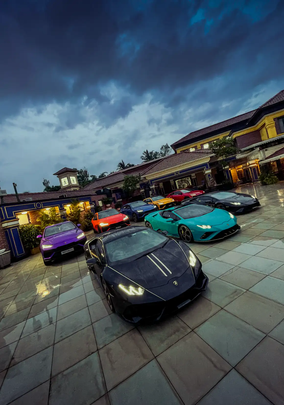 Lamborghini supercars gathered in a rain-soaked courtyard with a black Huracan leading the lineup