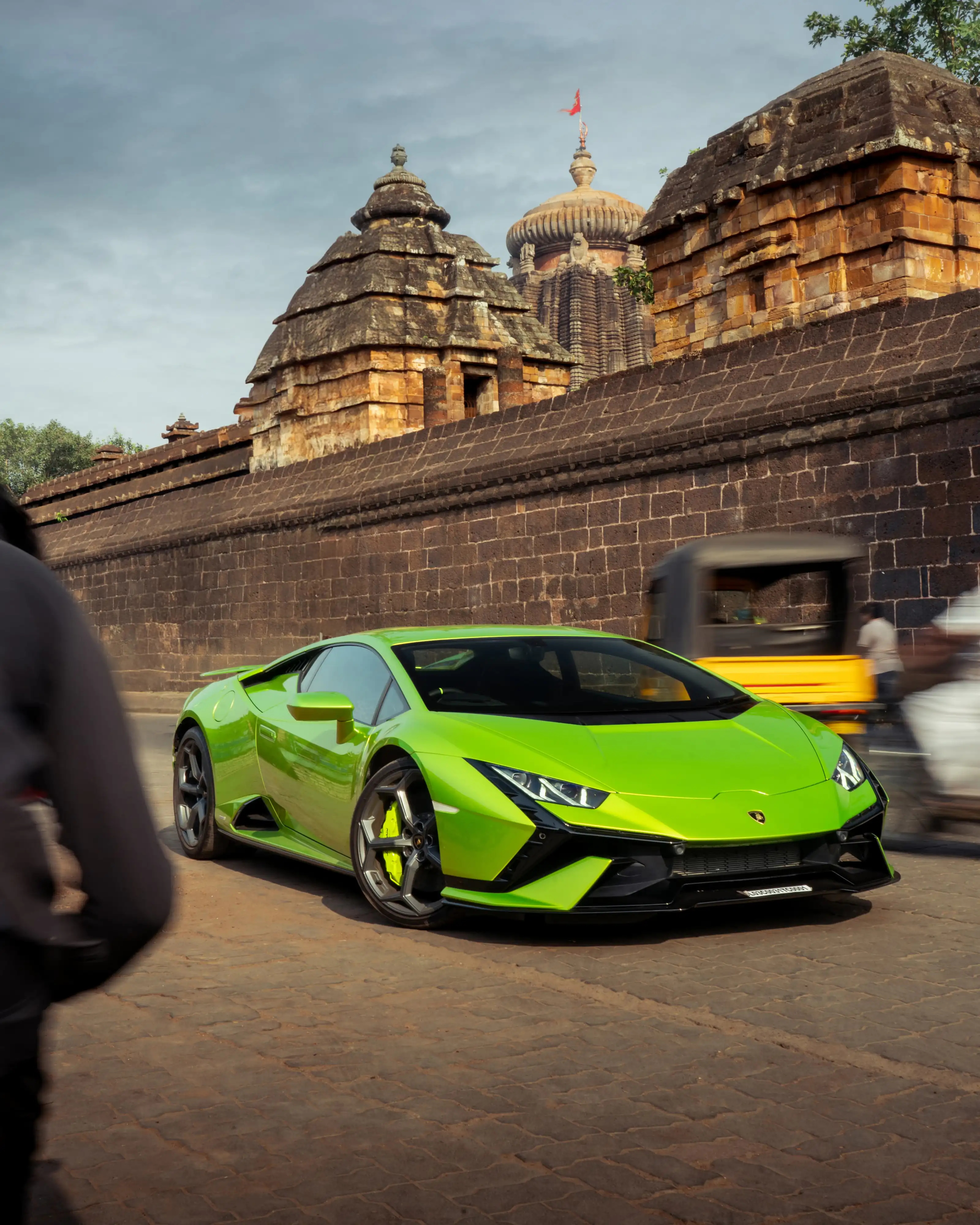 Bright green Lamborghini Huracan driving past a historic stone temple wall