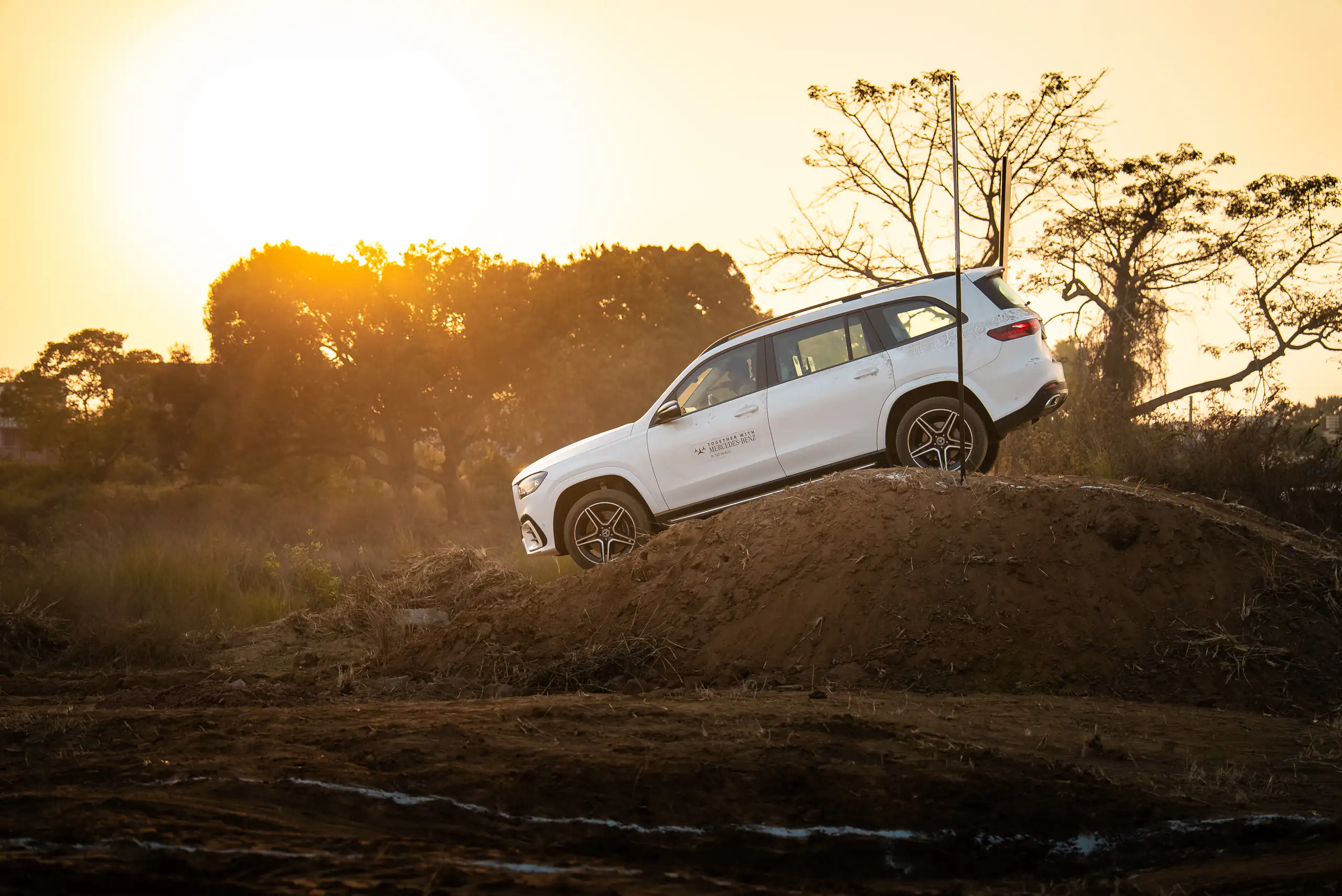White Mercedes-Benz SUV climbing a dirt ridge at sunset