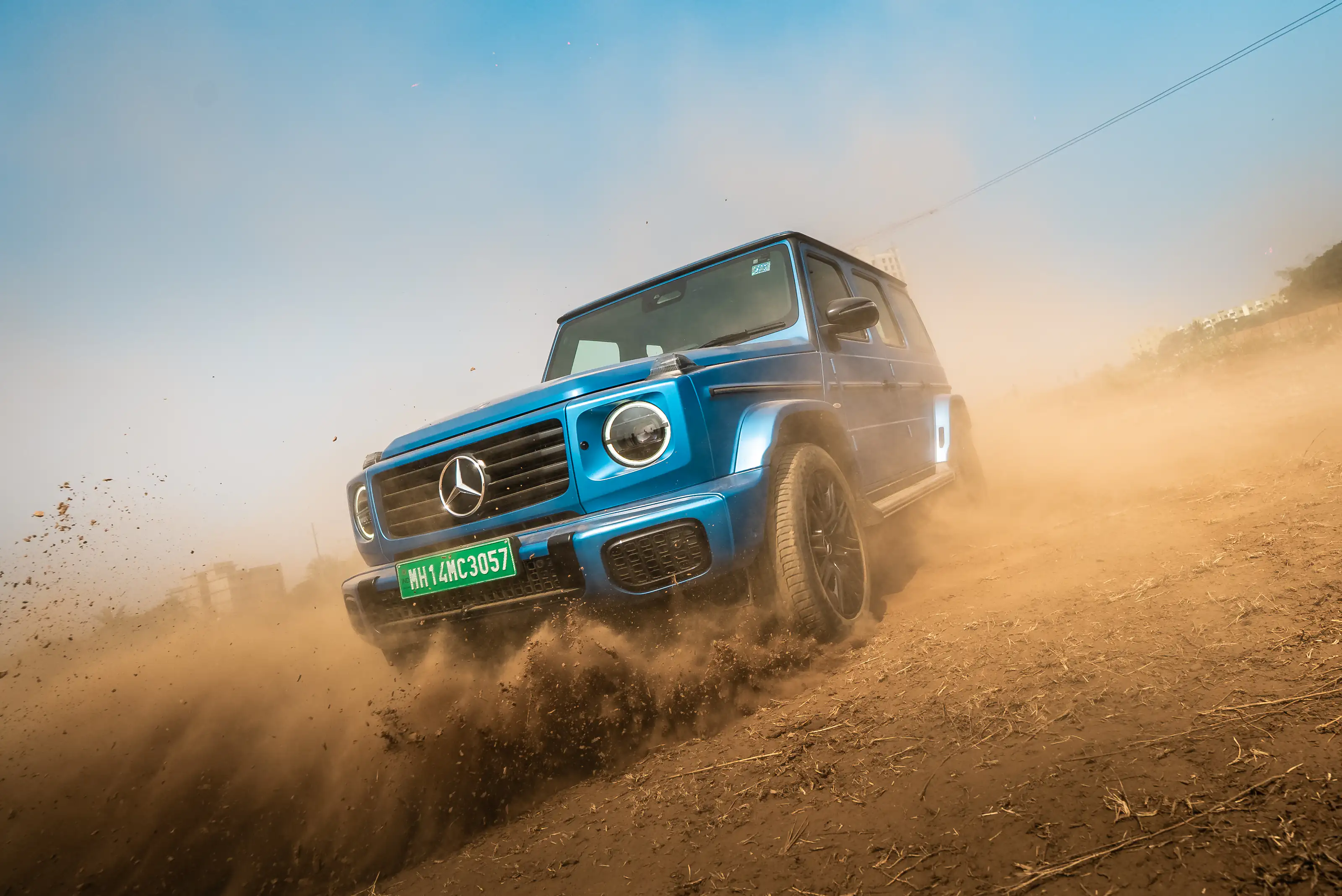 Blue Mercedes-Benz G-Class driving through dust on an off-road track