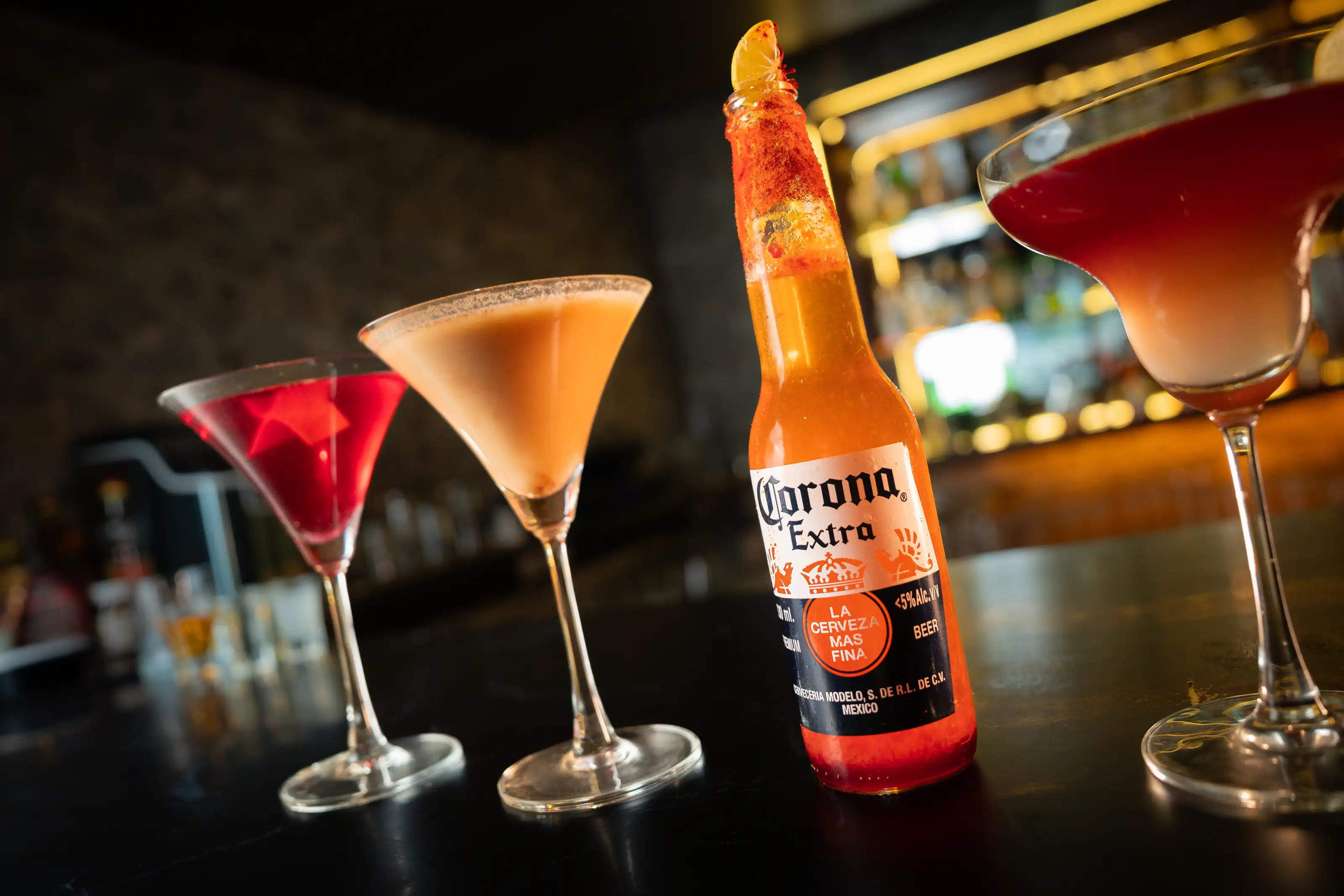 Colourful cocktails and a beer bottle arranged across a bar