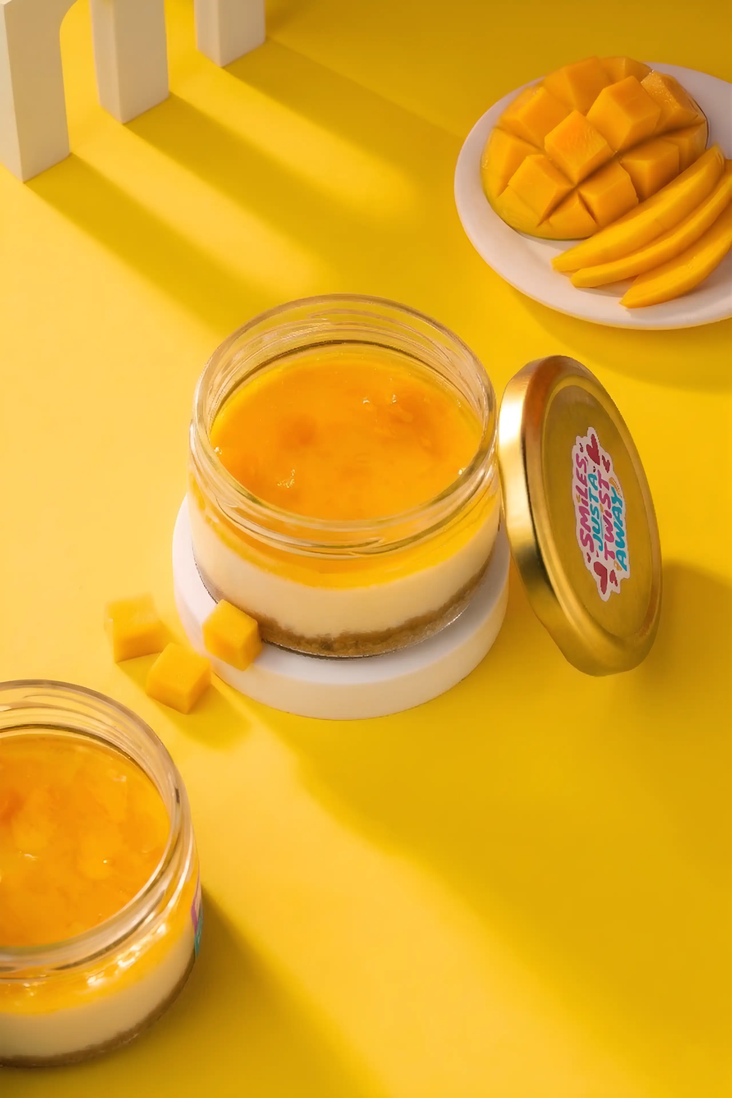 Layered mango dessert jars styled with fresh mango on a vivid yellow studio set