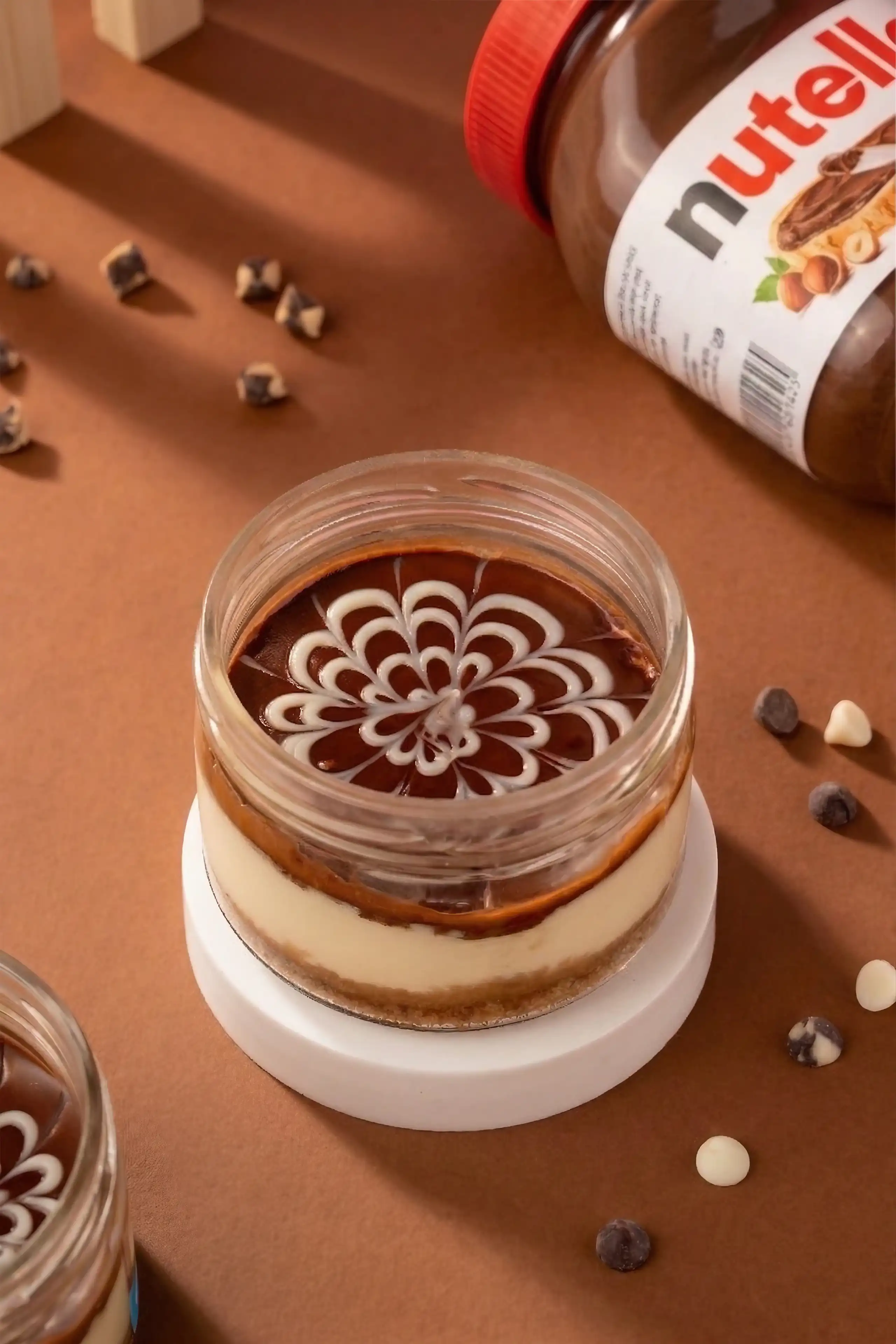 Layered chocolate and cream dessert topped with a floral swirl beside a Nutella jar