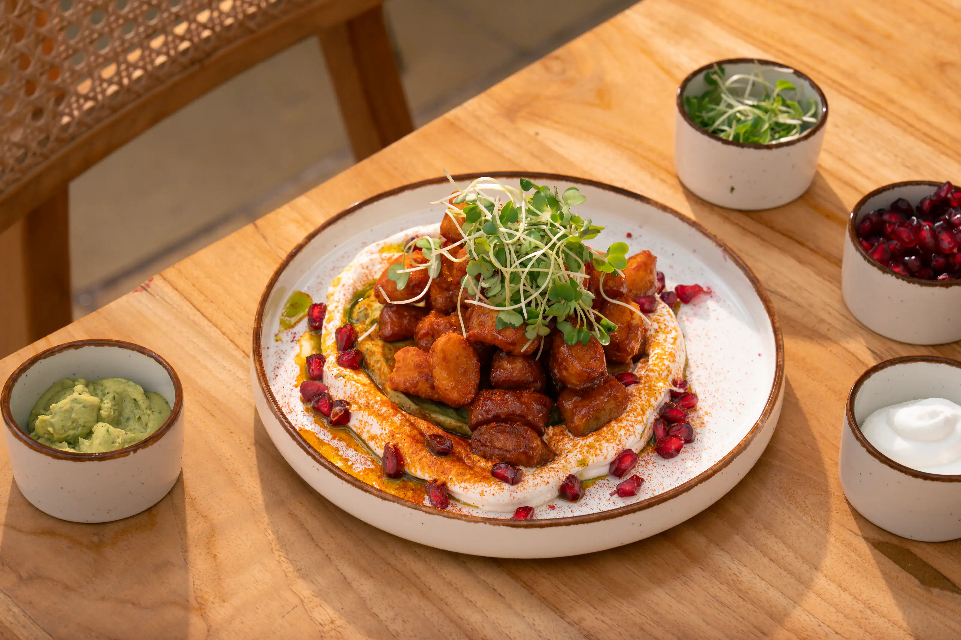 Crisp fried bites arranged over hummus with herbs and pomegranate on a sunlit table