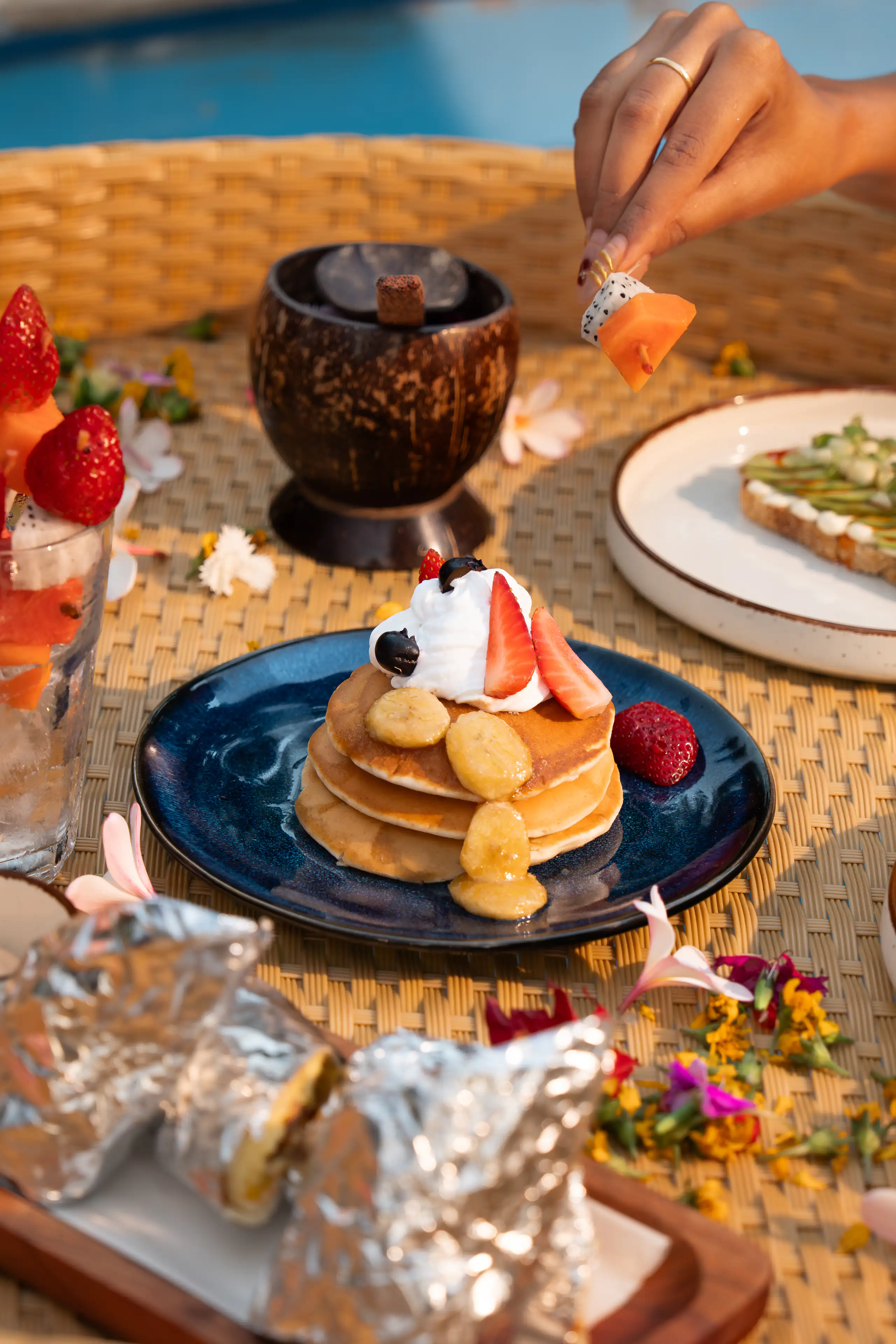 Pancakes, fruit and breakfast dishes arranged on a woven table