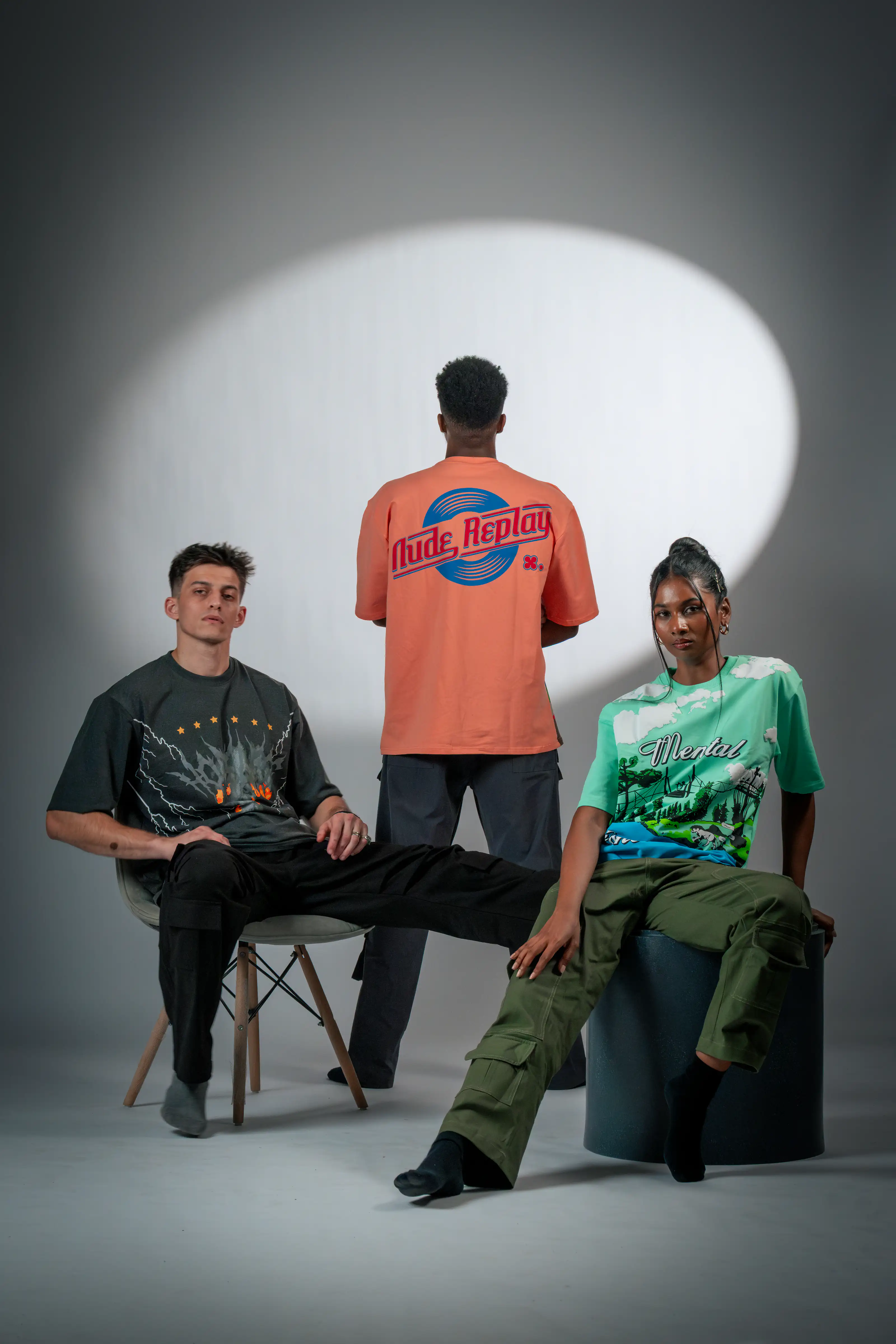 Three fashion models in graphic streetwear arranged beneath an oval studio light