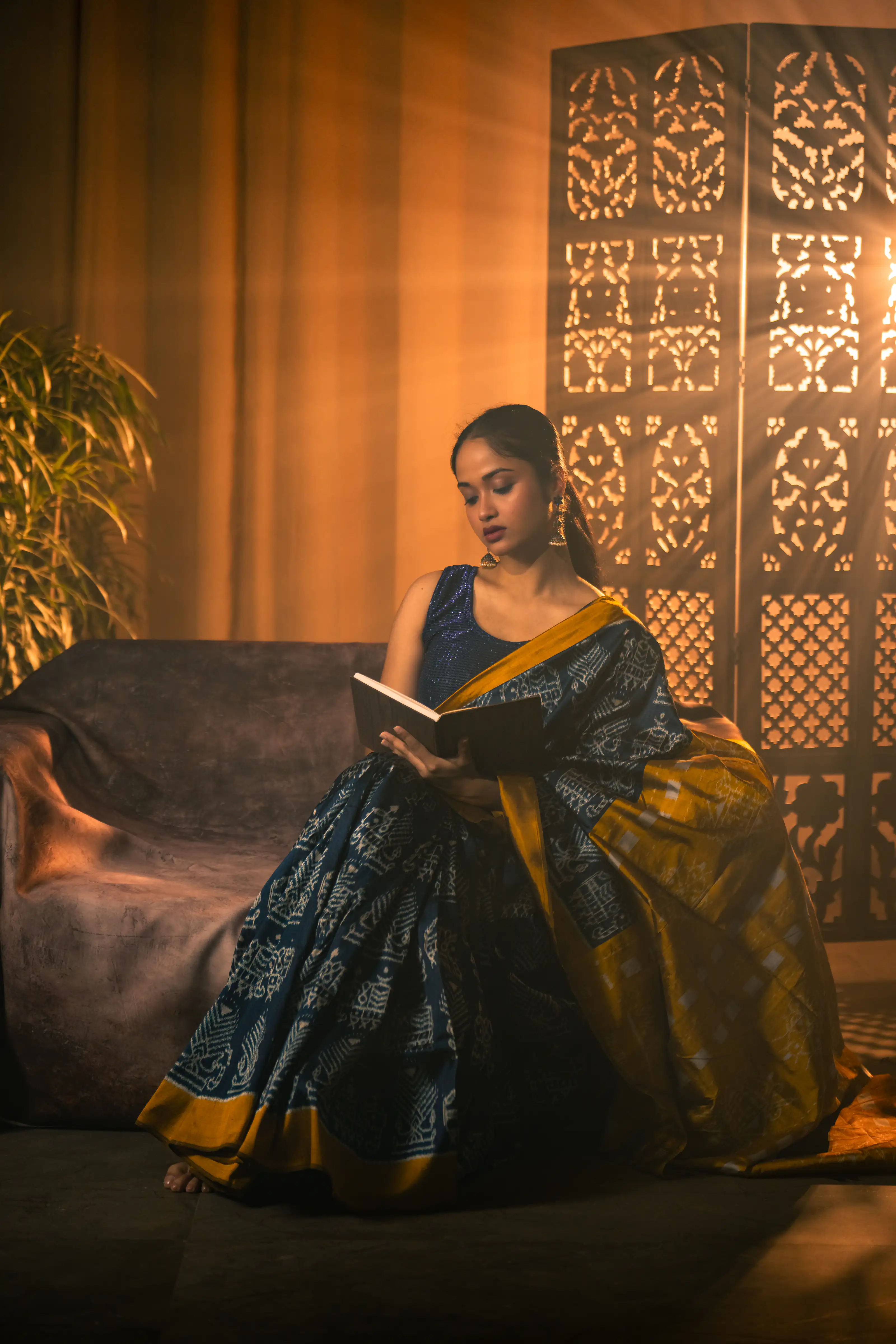 Woman in a blue and gold sari reading on a sofa in a warmly lit room