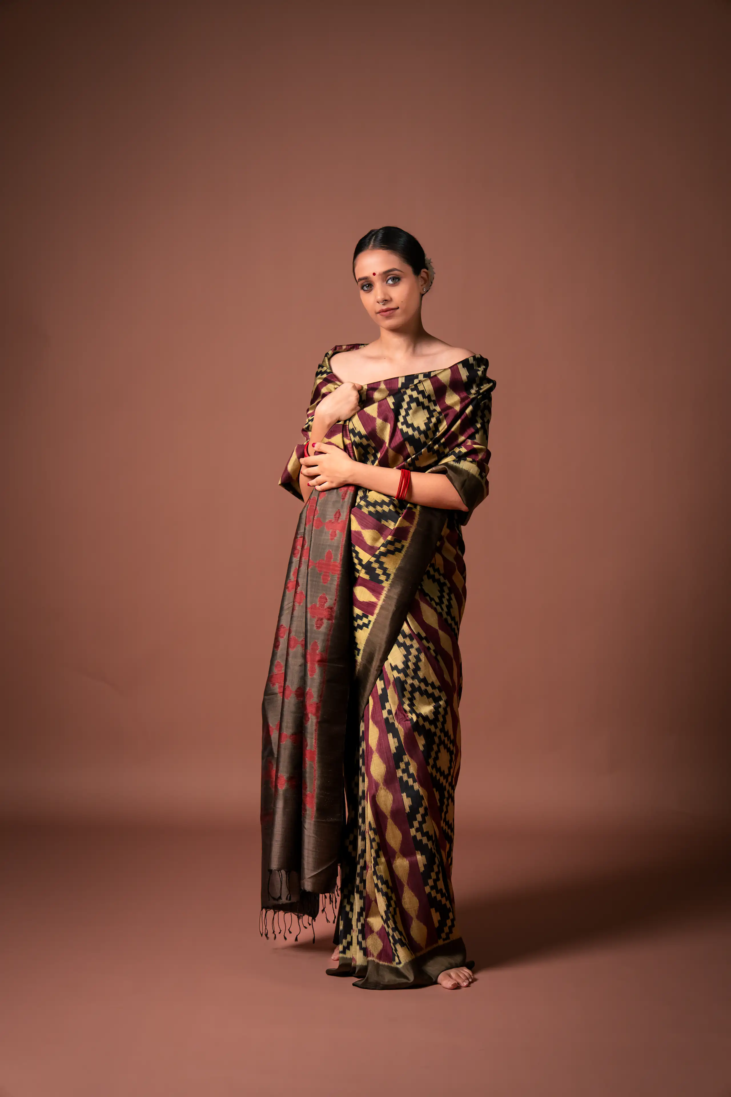 Woman in a patterned sari posed against a soft terracotta studio background