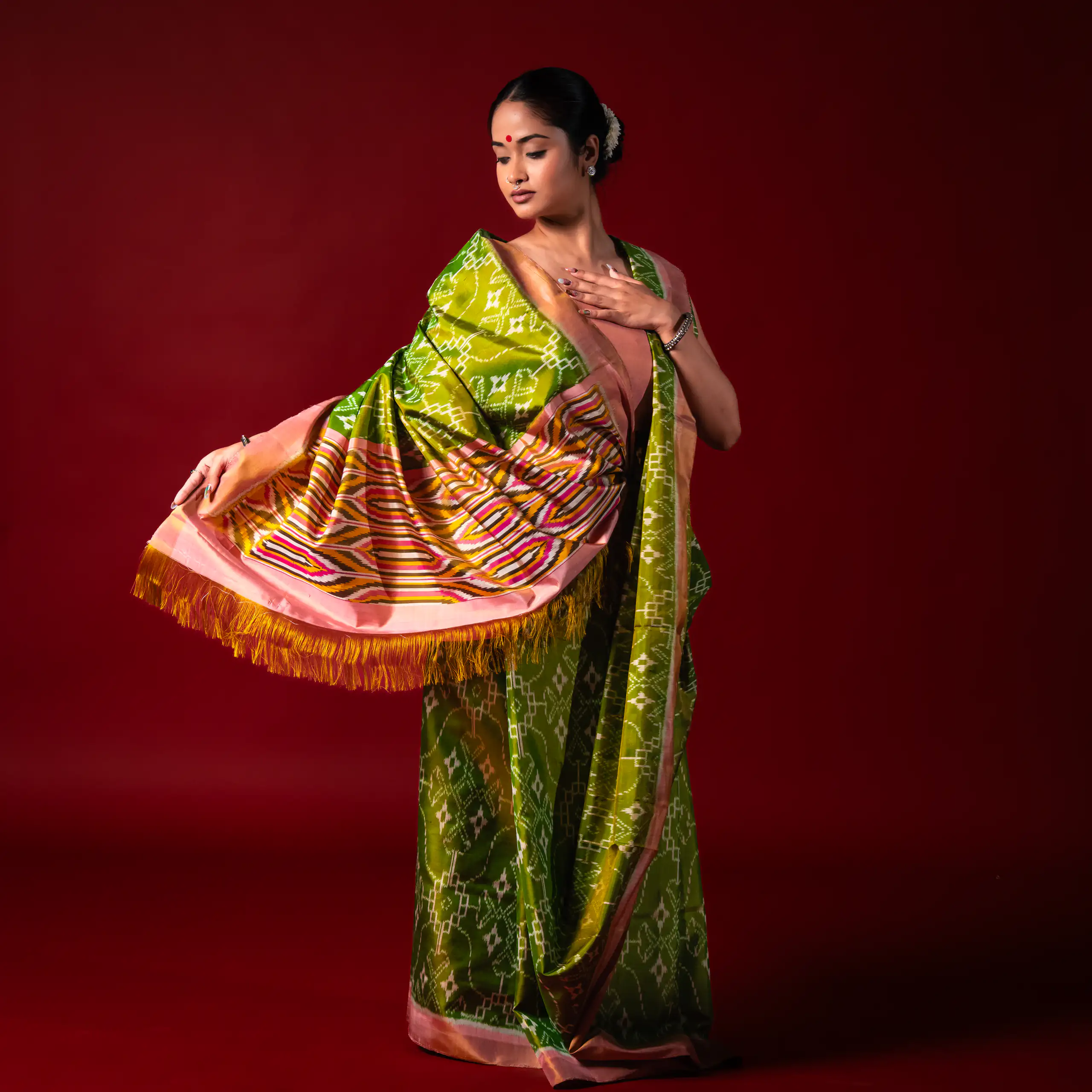 Woman in a vivid green patterned sari seated against a red studio backdrop