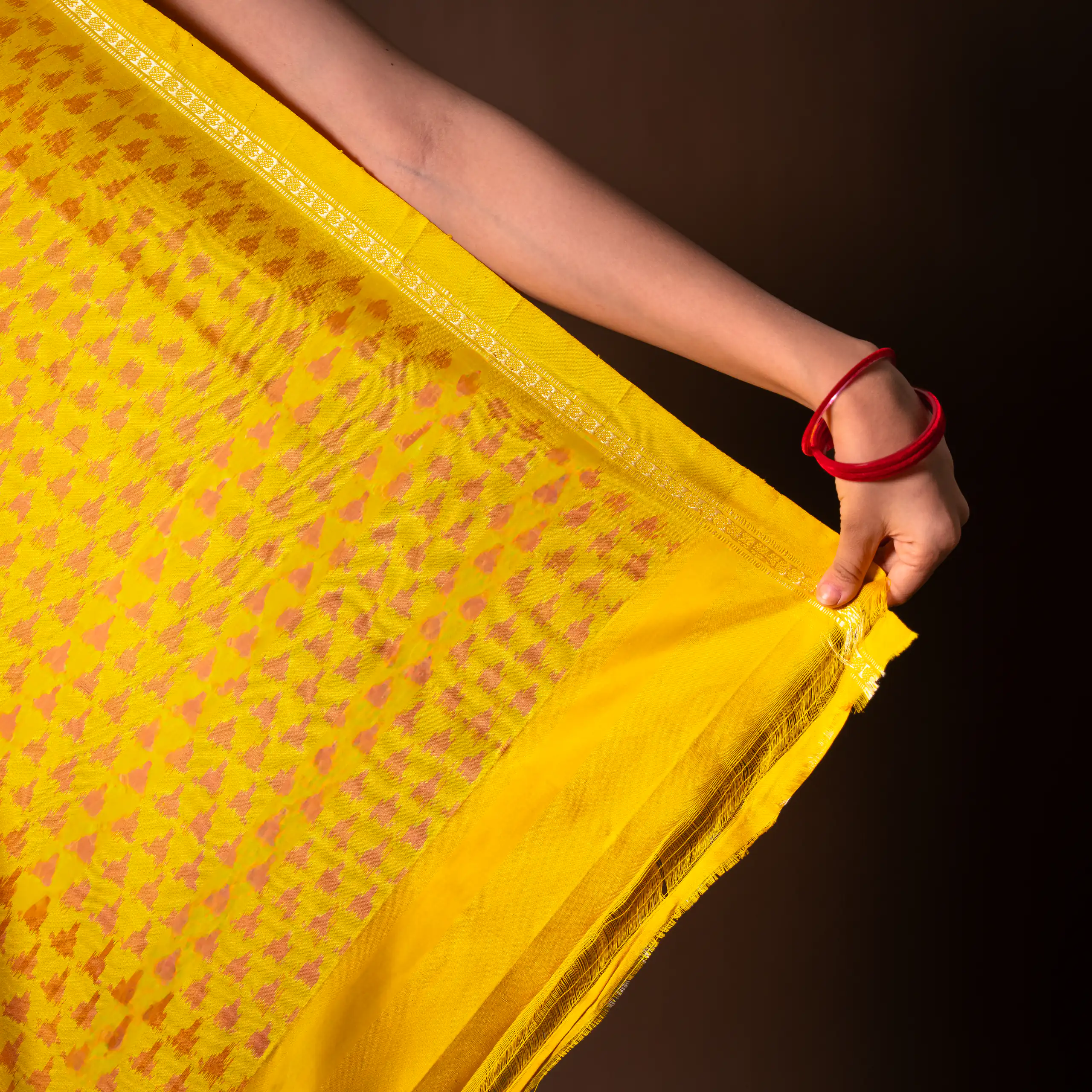 Close fashion detail of a yellow patterned sari and red bangles
