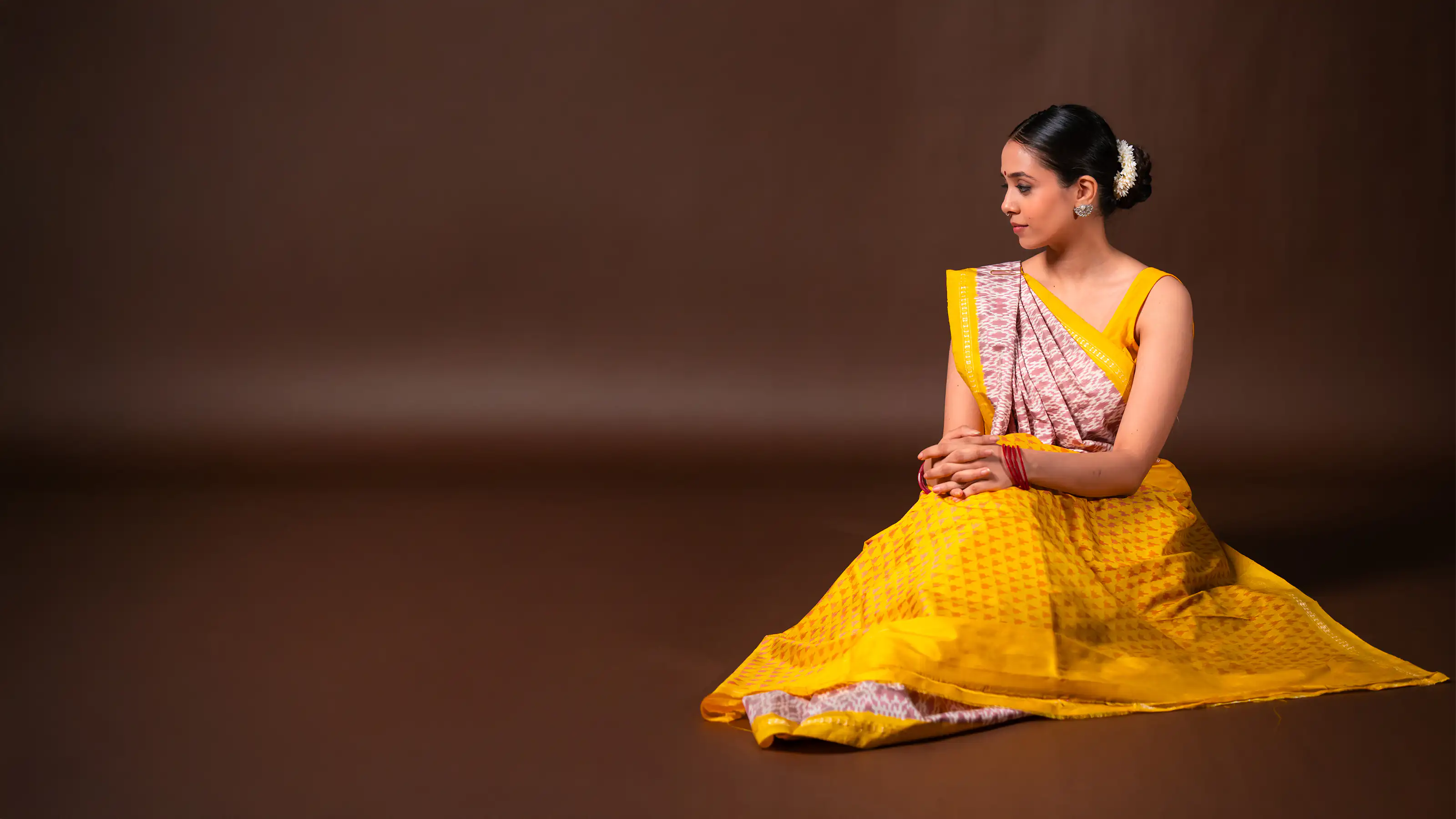 Model in a yellow and pink ikat sari seated against a warm brown studio backdrop