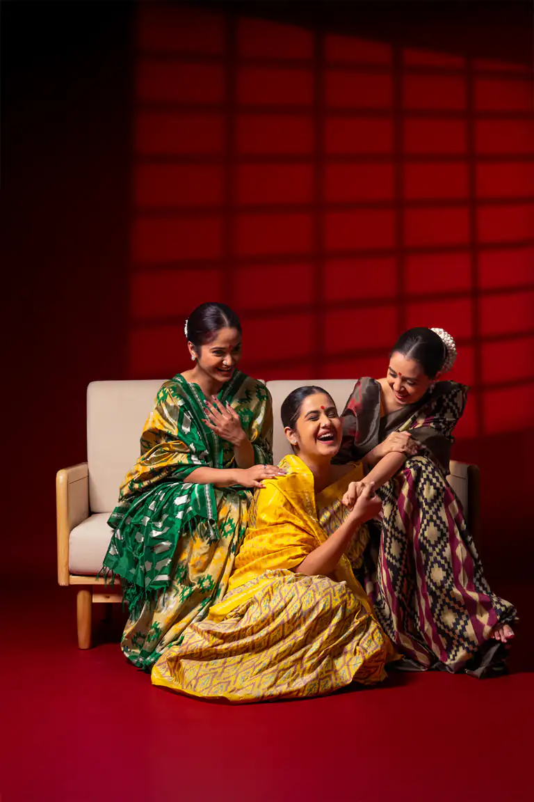 Three models in patterned saris laughing together on a red studio set