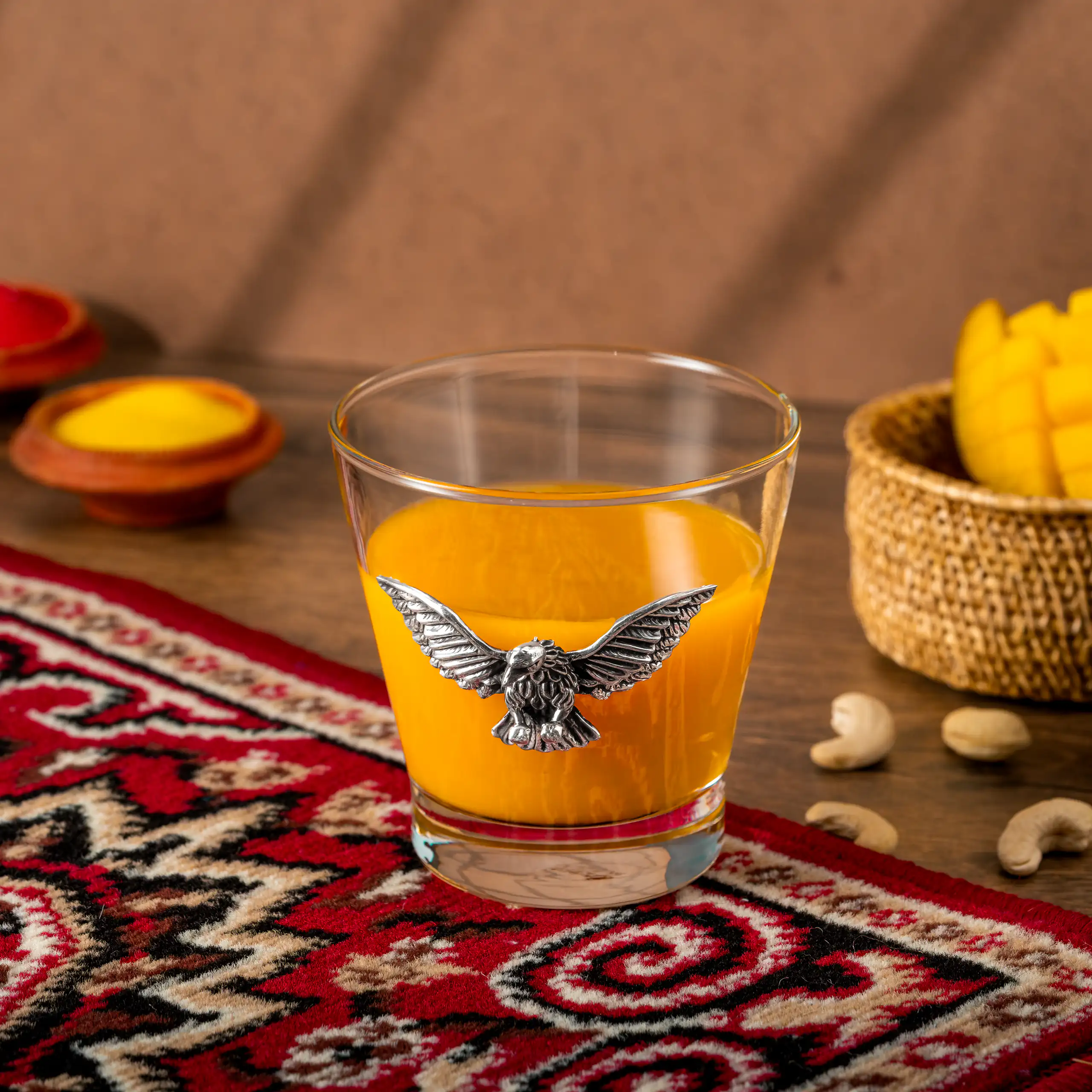 Amber drink in a glass with an eagle emblem styled on a richly patterned table