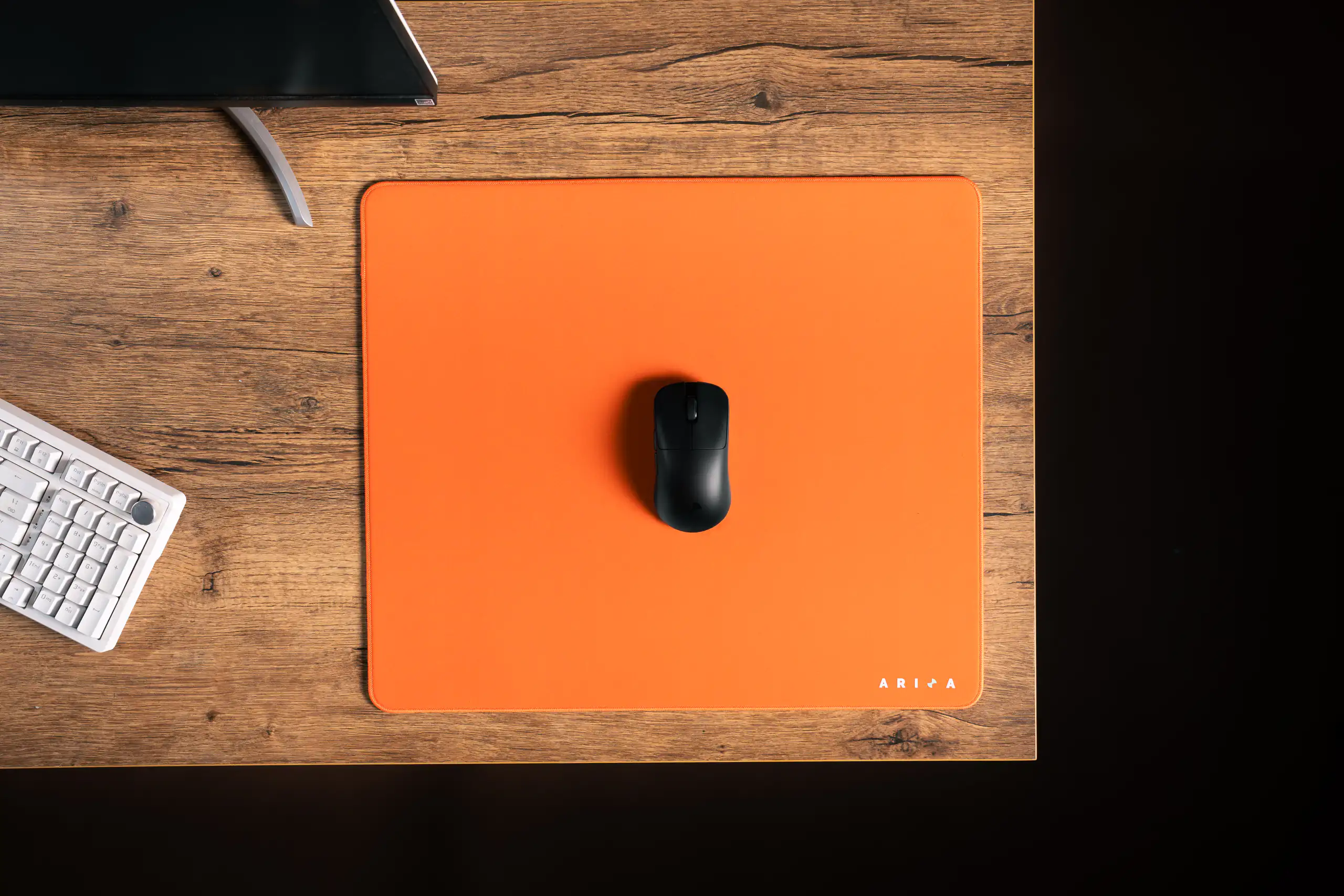 Black computer mouse centered on an orange desk mat in a graphic overhead composition