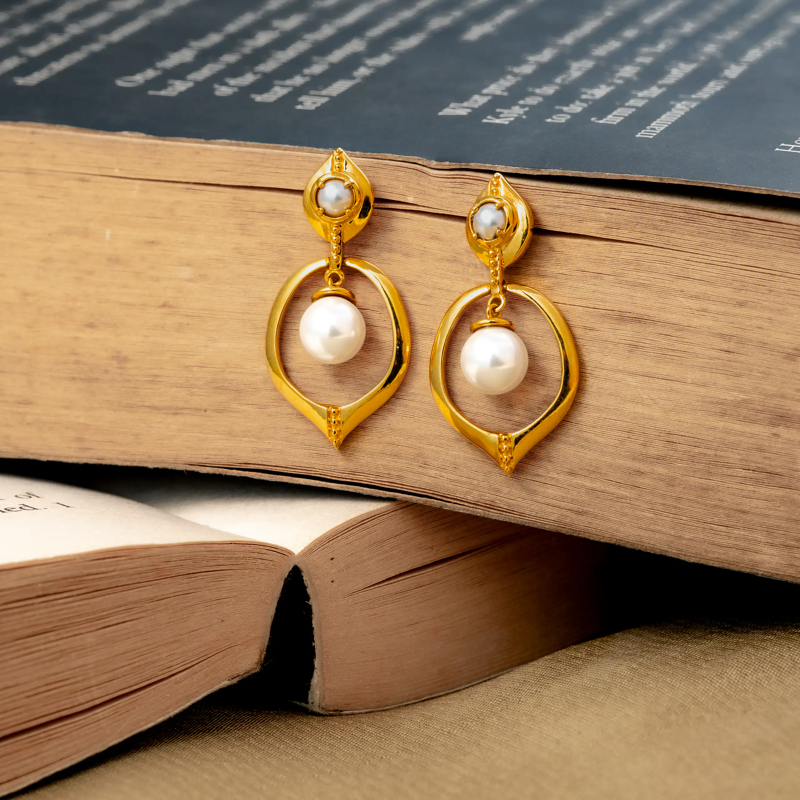 Gold and pearl drop earrings arranged across open books on a wooden table