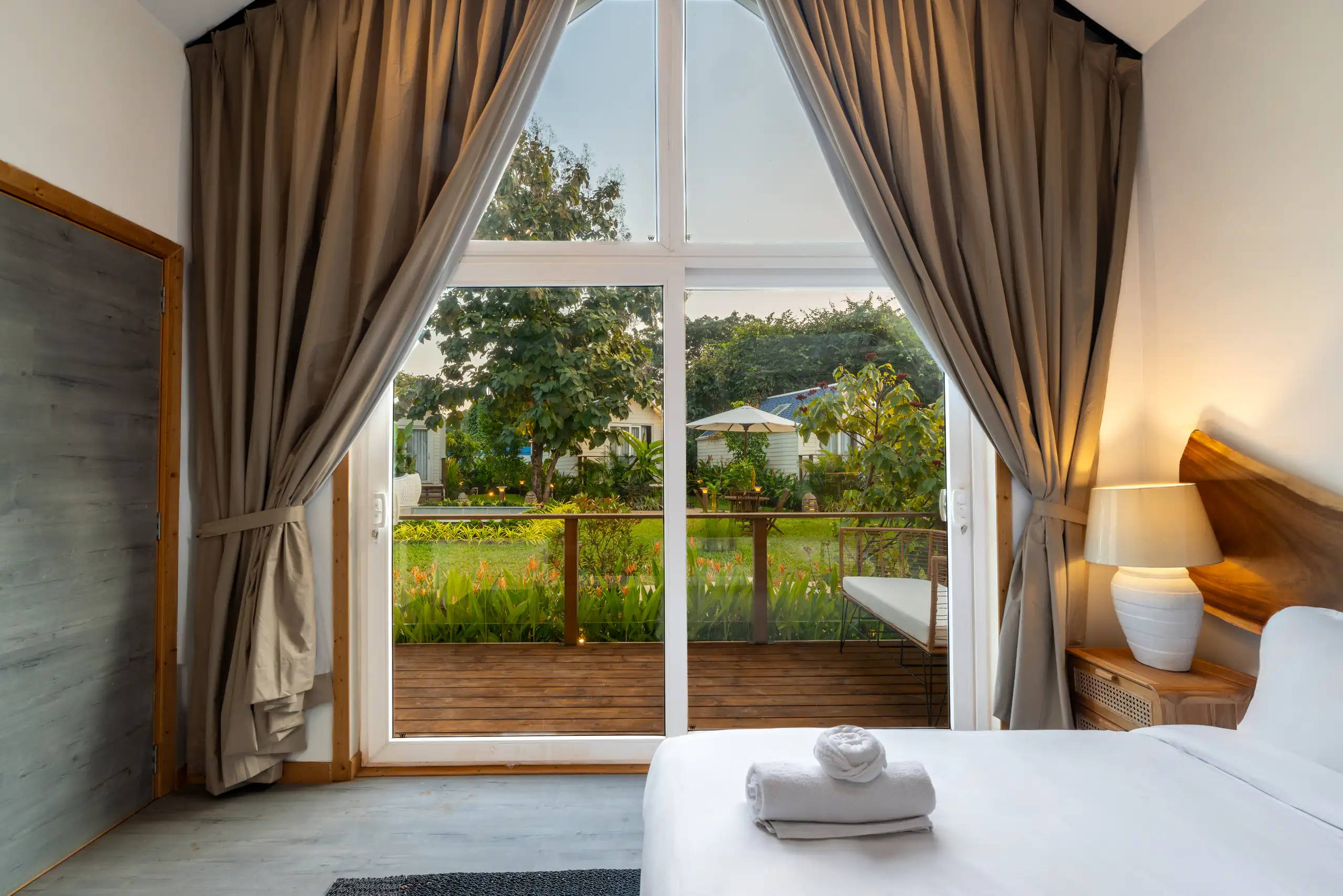 Resort bedroom opening through tall curtains onto a green garden