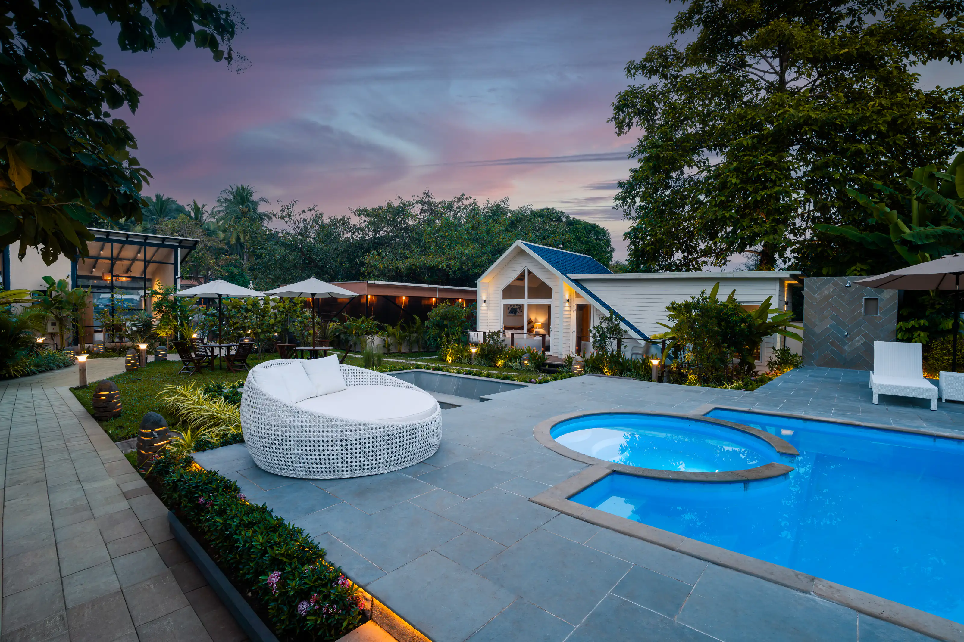 Resort courtyard with a bright blue pool and white loungers at dusk
